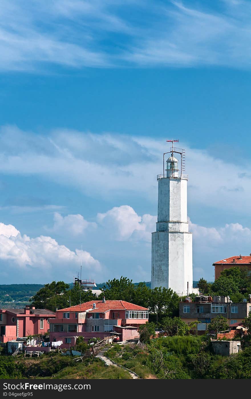 Vertical photo of a white lighthouse. It is located in the city and there are buildings around it. The sky is vivid and there are clouds. Vertical photo of a white lighthouse. It is located in the city and there are buildings around it. The sky is vivid and there are clouds.