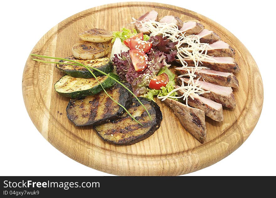 Meat roasted on a grill with vegetables on a wooden plate