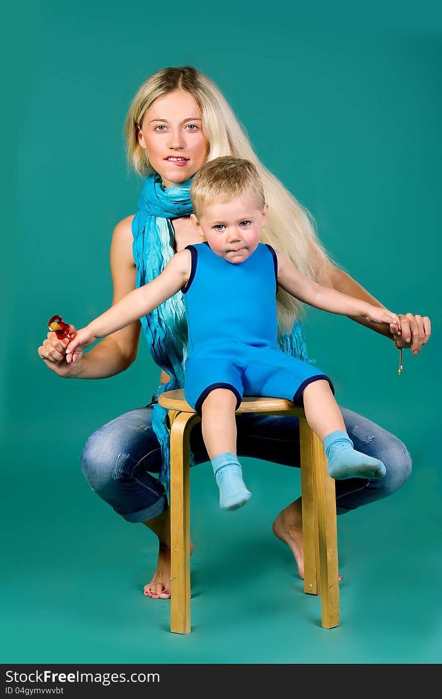 Portrait of blonde mom in jeans and a scarf and a son in a blue suit, a green background. Portrait of blonde mom in jeans and a scarf and a son in a blue suit, a green background