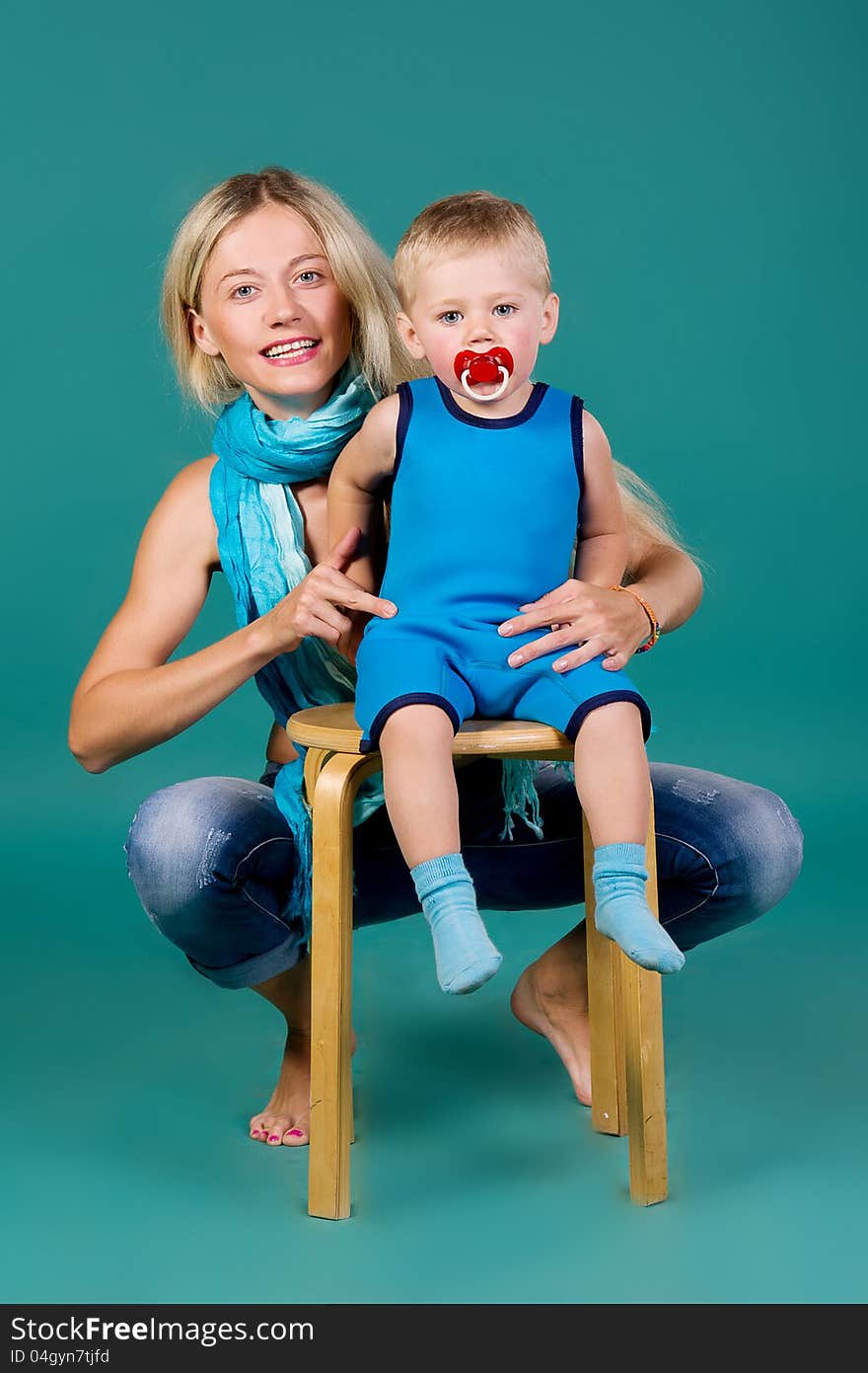 Portrait of blonde mom in jeans and a scarf and a son in a blue suit, a green background. Portrait of blonde mom in jeans and a scarf and a son in a blue suit, a green background