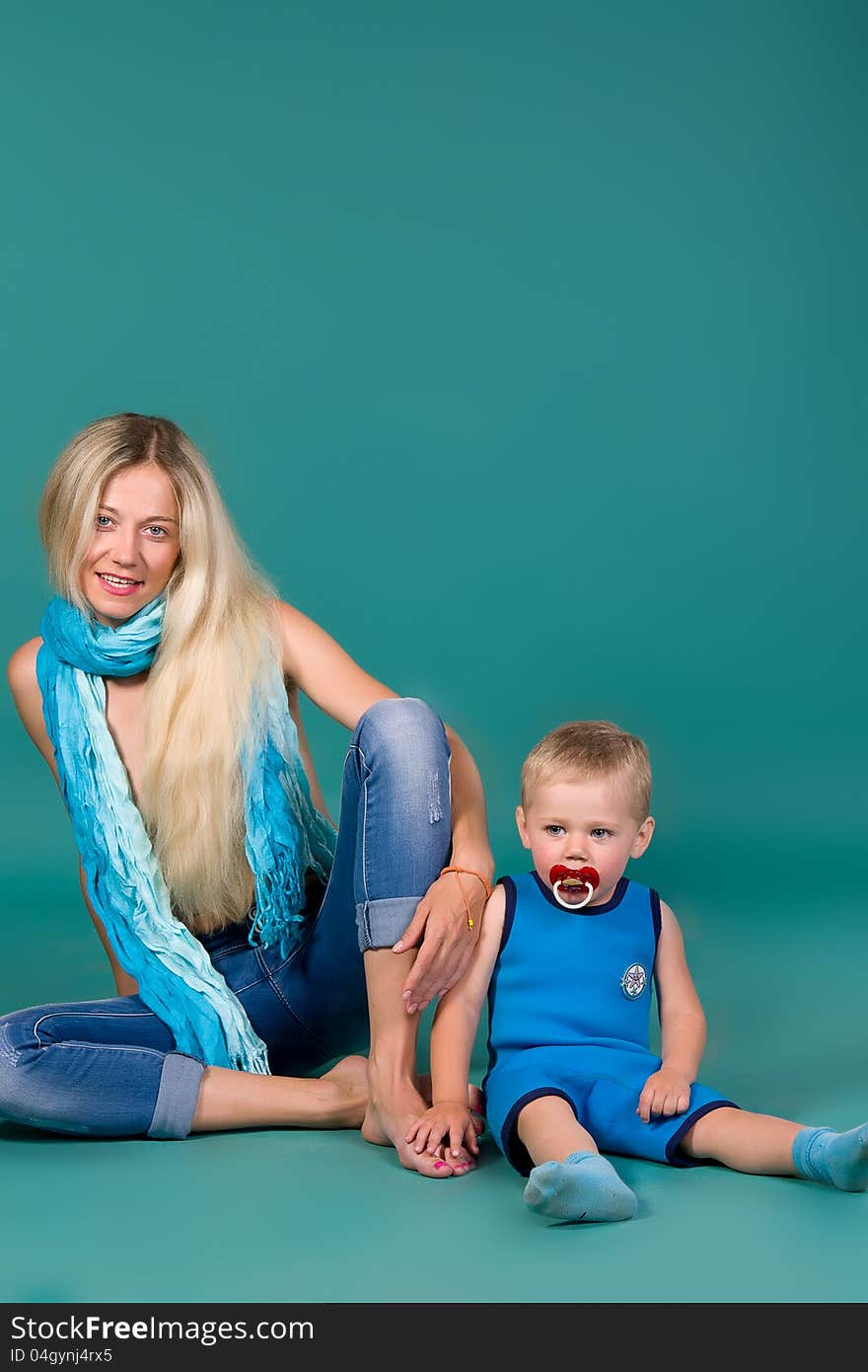 Portrait of blonde mom in jeans and a scarf and a son in a blue suit, a green background. Portrait of blonde mom in jeans and a scarf and a son in a blue suit, a green background