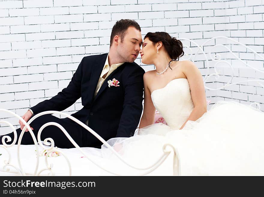 Bride and groom sitting on bed in bedroom