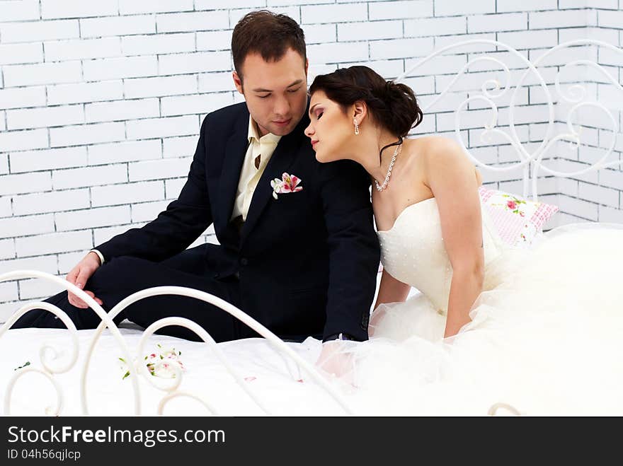 Bride and groom sitting on bed in stylish bedroom. Bride and groom sitting on bed in stylish bedroom