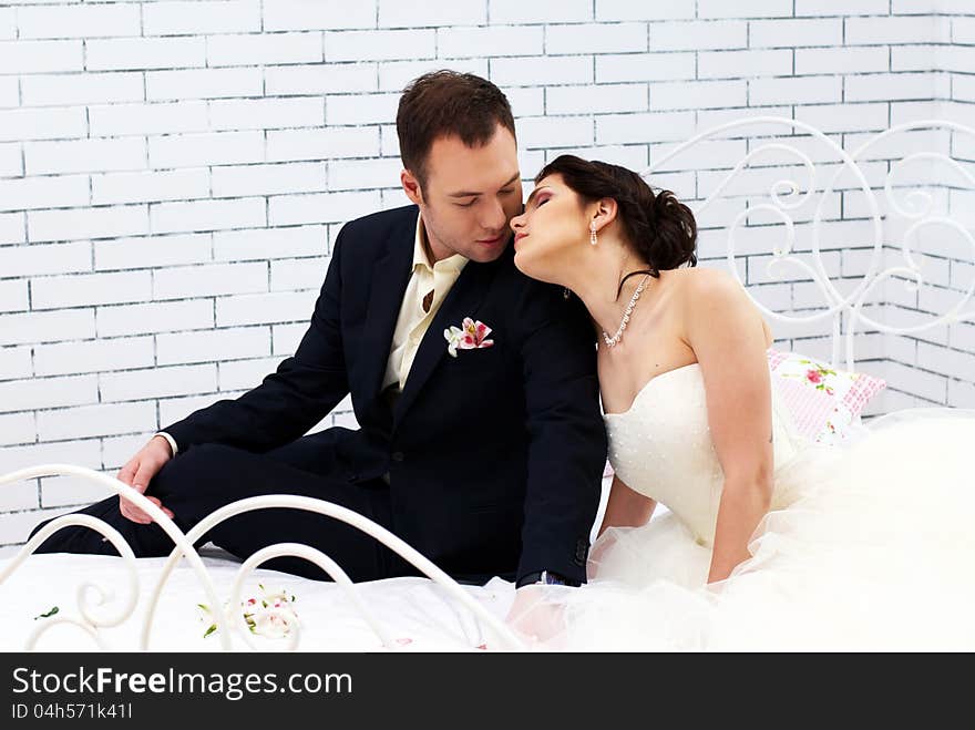 Bride And Groom Sitting On Bed In Bedroom