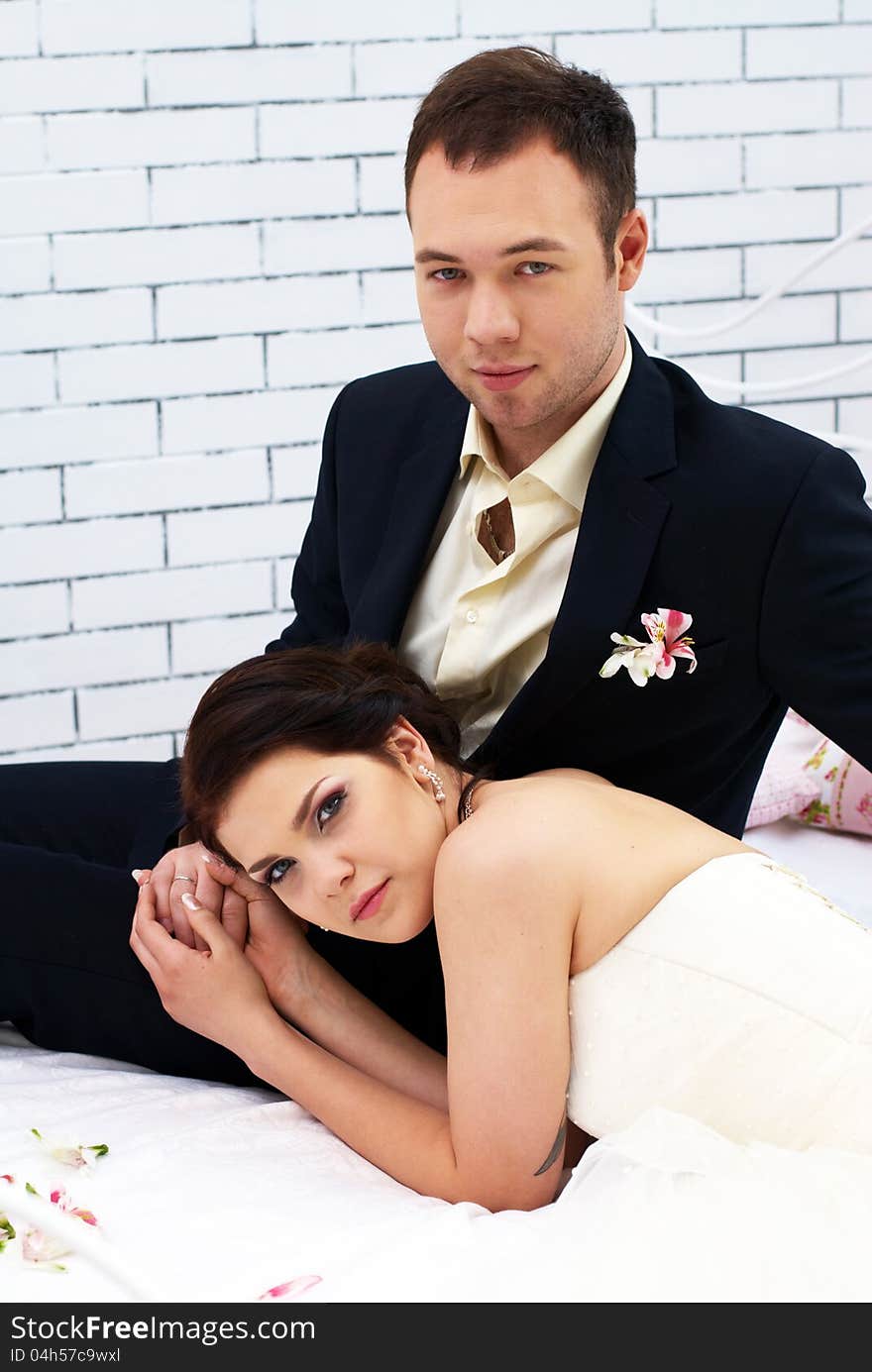 Bride and groom sitting on bed in bedroom