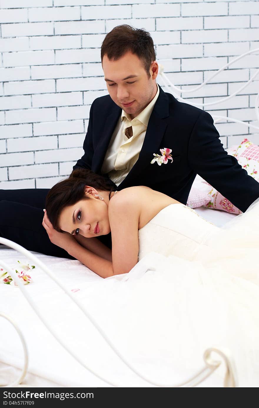 Bride and groom sitting on bed in bedroom