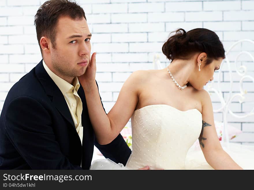 Bride And Groom Sitting On Bed In Bedroom