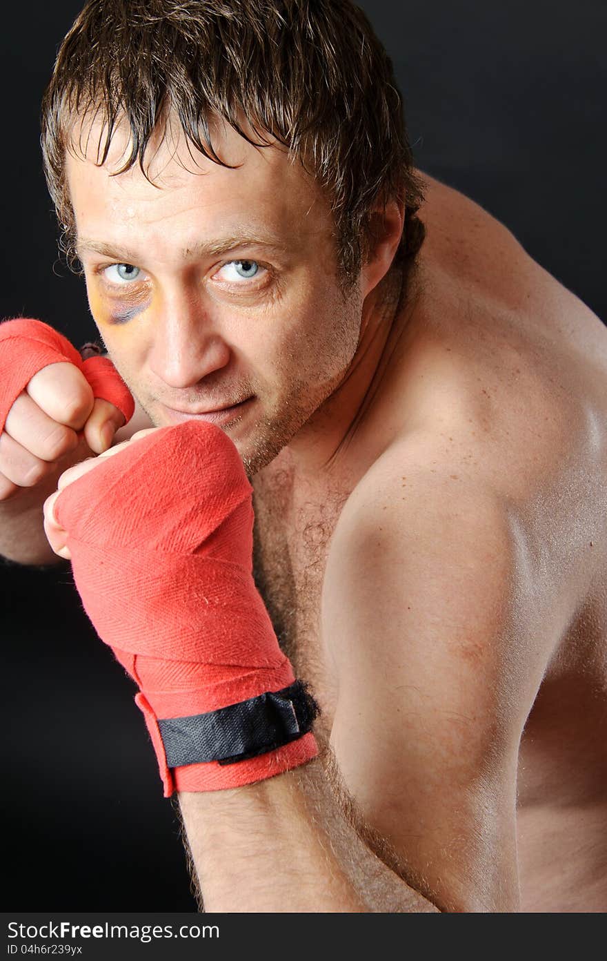 Portrait of a man with a bruise in a battle position. Clenched fists. Dark background. Portrait of a man with a bruise in a battle position. Clenched fists. Dark background.