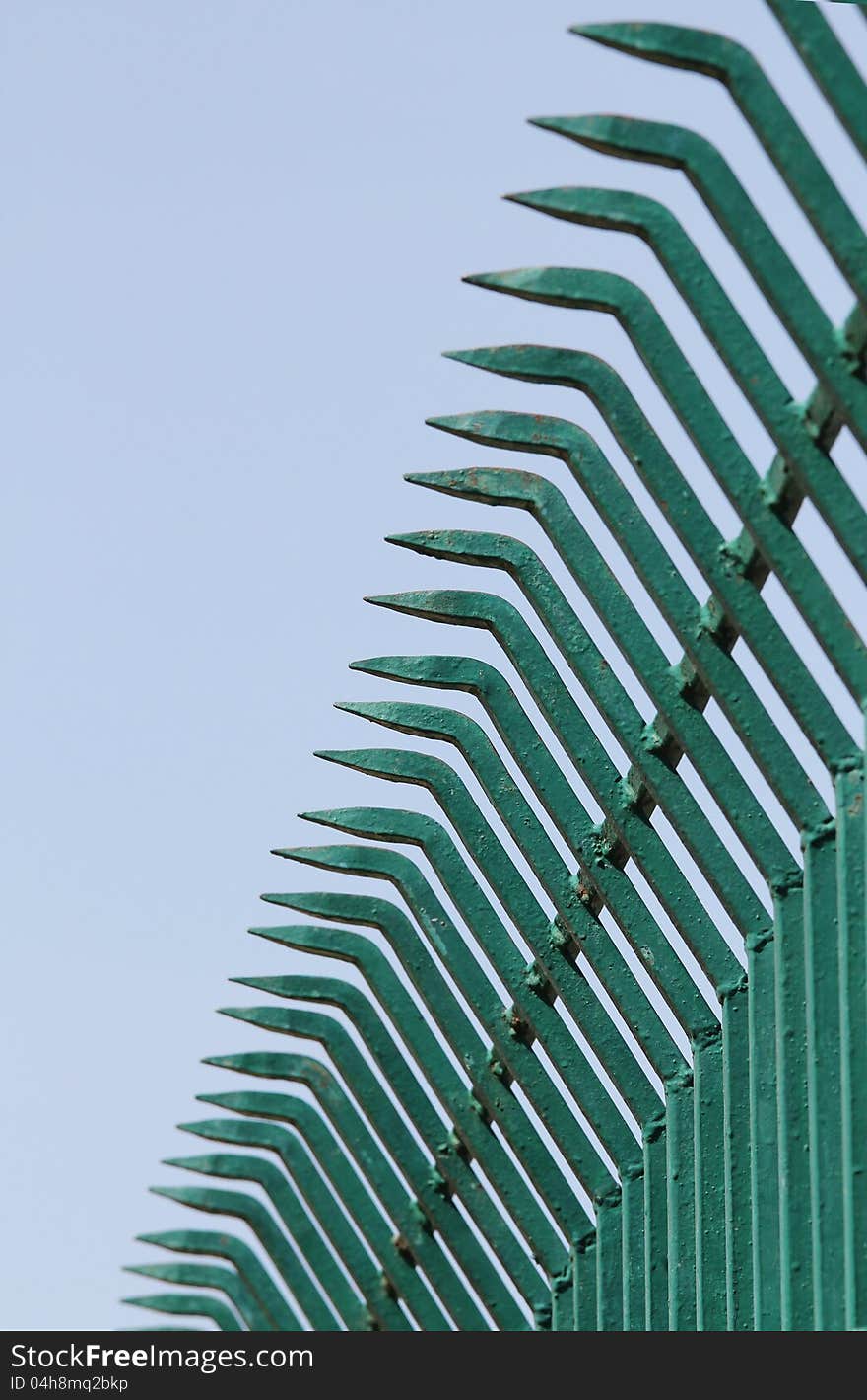 Rows of pointed sharp wrought iron bars forged to form a fence in green color and sky in the background. Rows of pointed sharp wrought iron bars forged to form a fence in green color and sky in the background