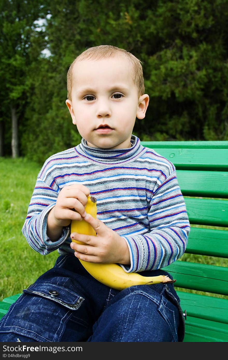 Boy outdoors sitting on a bench and cleans the banana. Boy outdoors sitting on a bench and cleans the banana