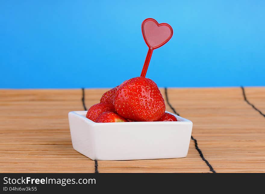 White dish with ripe fresh strawberries on a bamboo table