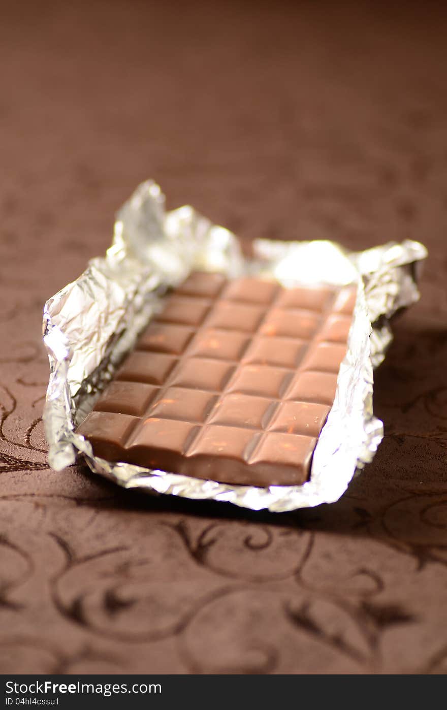 Chocolate bar in tinfoil on brown background