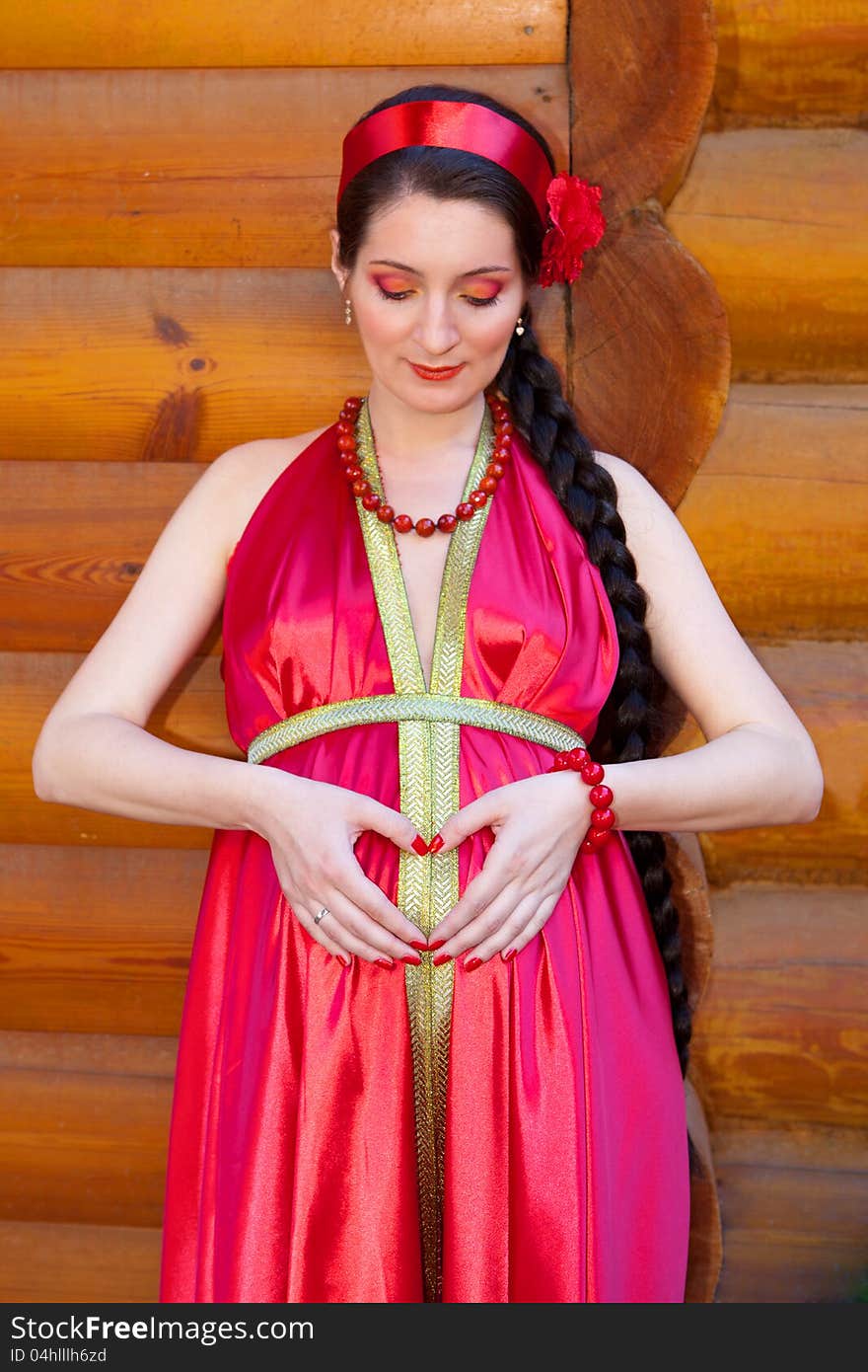 A young girl in a red dress, holding her hand in the shape of a heart on her pregnant belly