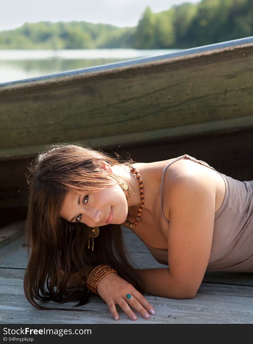 An image gorgeous young woman, smiling sweetly at the viewer, lying on a dock with a boat and lake behind her. An image gorgeous young woman, smiling sweetly at the viewer, lying on a dock with a boat and lake behind her