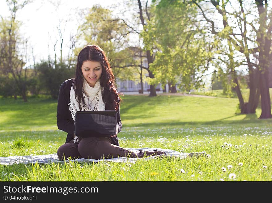 Young woman working with net-book outdoors in park on grass. Young woman working with net-book outdoors in park on grass