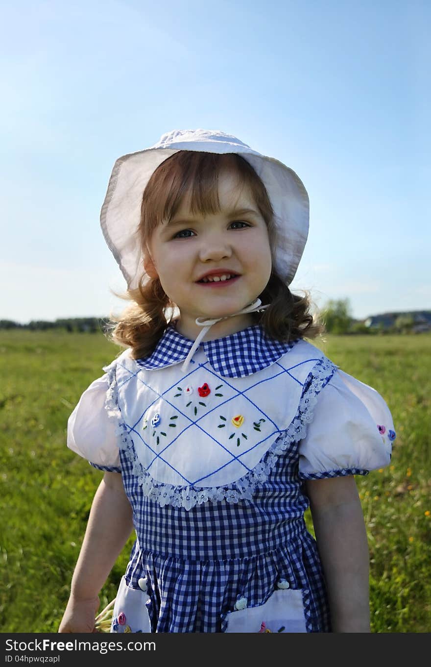 Happy little girl wearing dress and white panama stands on green field. Happy little girl wearing dress and white panama stands on green field