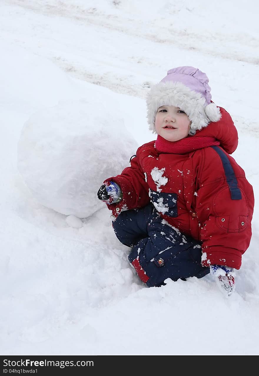 Little tired girl sits on snow near big snowball