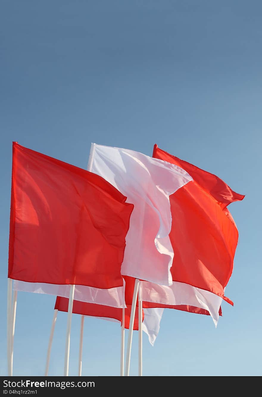 Eight red and white flags flutter in wind on blue sky background