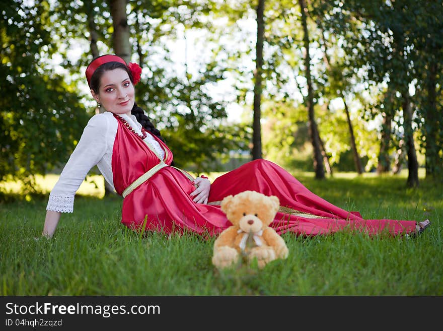 A young pregnant girl sitting on the grass in a red dress