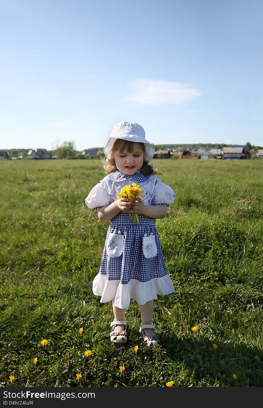 Little girl holds yellow dandelions on green field