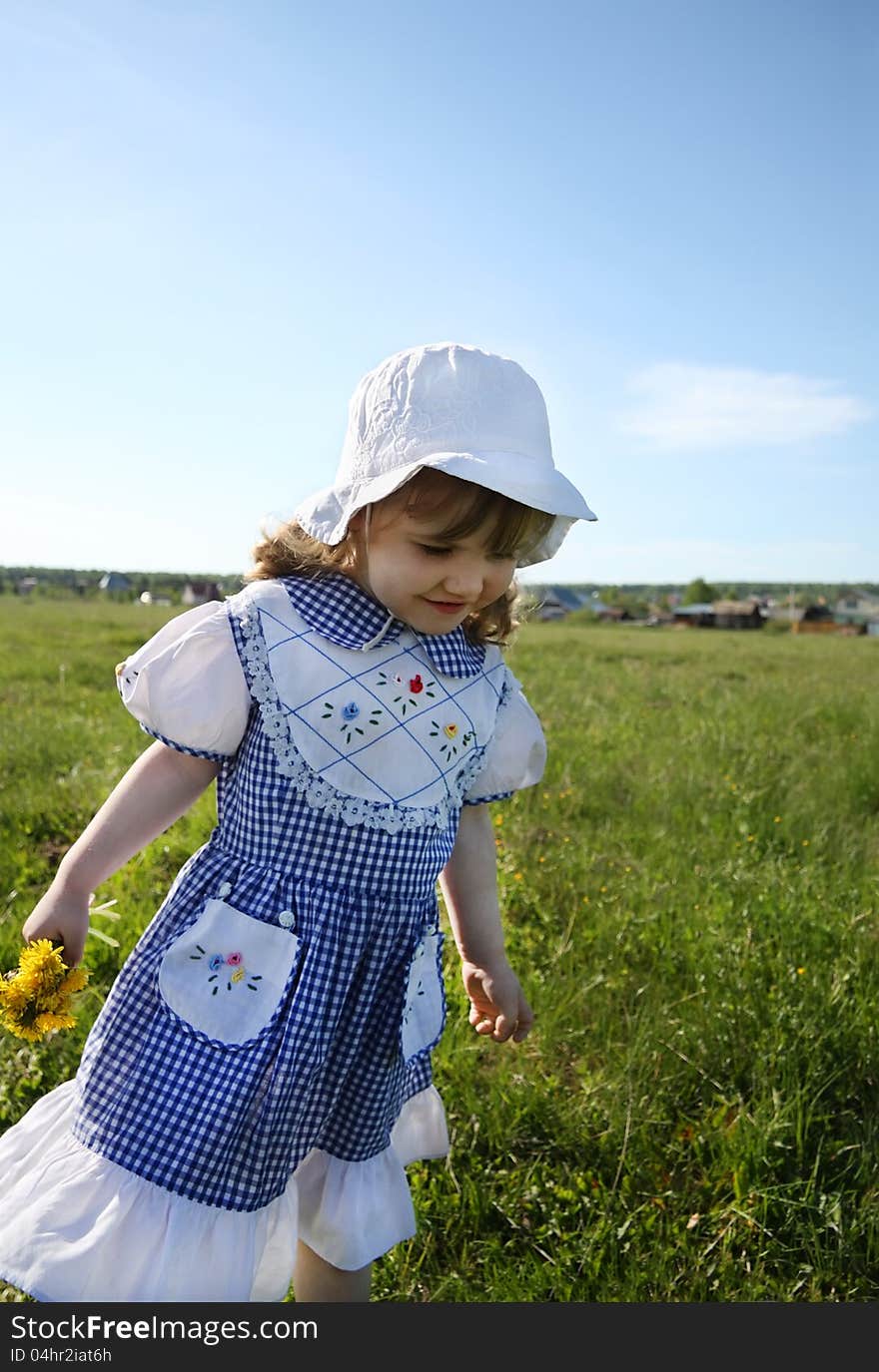 Happy little girl wearing dress and white panama walks on green field. Happy little girl wearing dress and white panama walks on green field