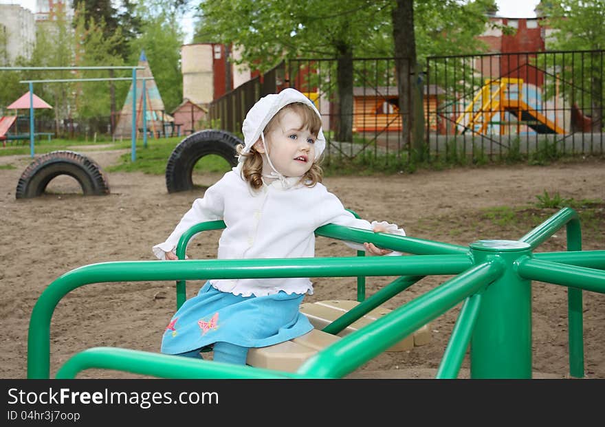 Pensive little girl wearing white panama rides on small carousel at playground. Pensive little girl wearing white panama rides on small carousel at playground