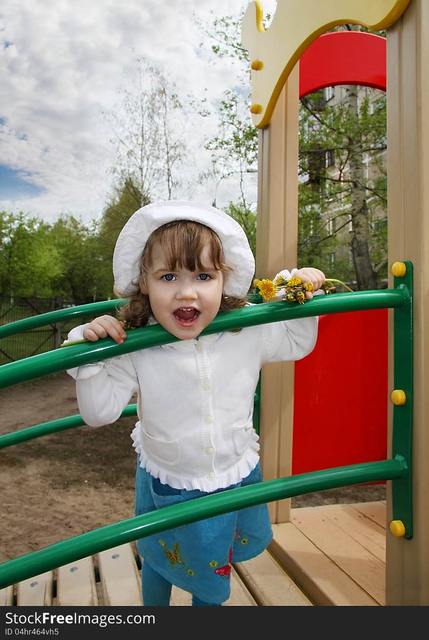 Cute little girl wearing white blouse stands on playground and looks at camera. Cute little girl wearing white blouse stands on playground and looks at camera