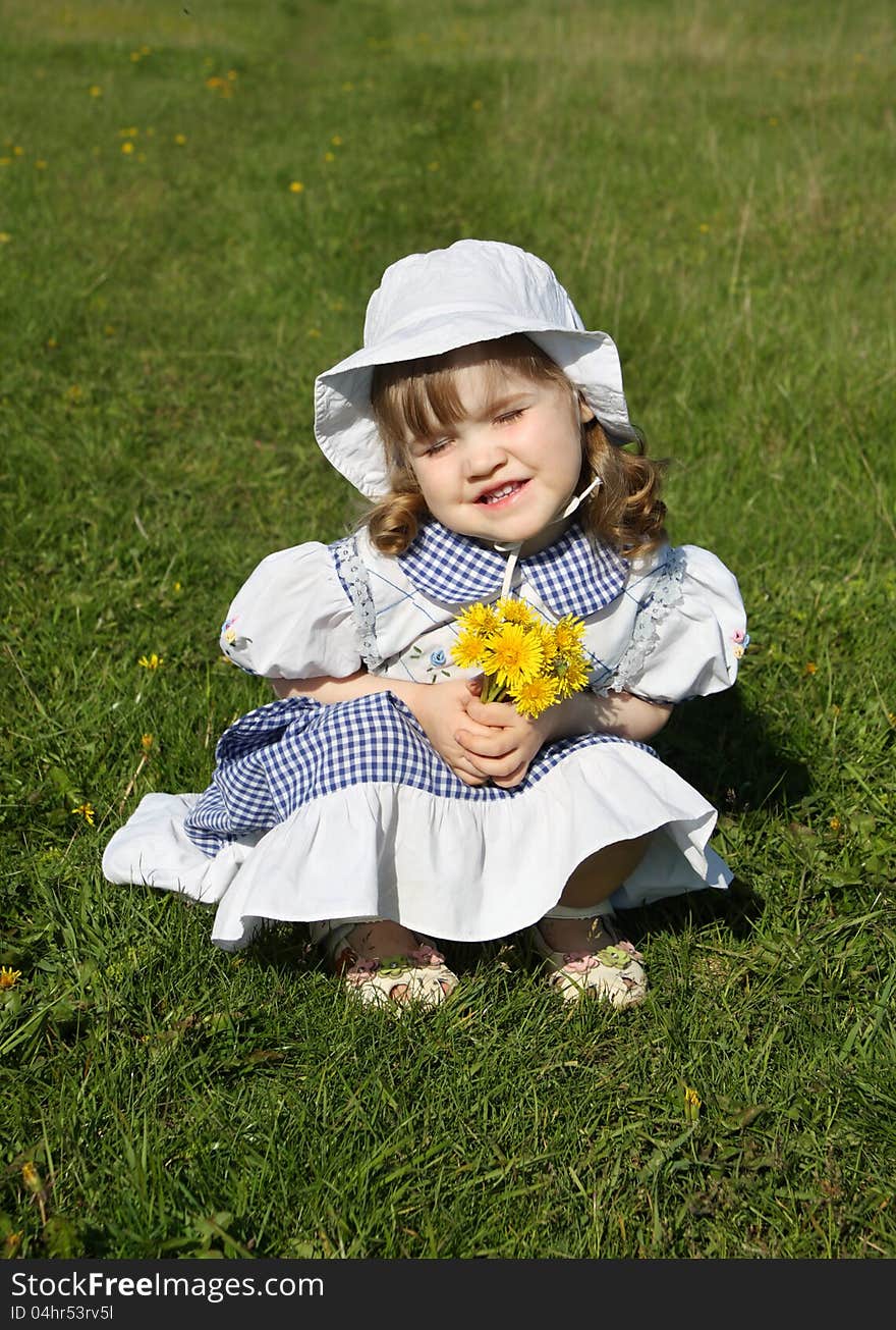 Little girl with yellow dandelions sits on grass