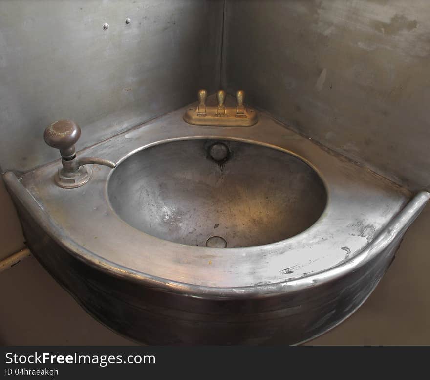 Old corner single stainless steel metal sink with brass controls and single tap. From an old train car lavatory. Old corner single stainless steel metal sink with brass controls and single tap. From an old train car lavatory.