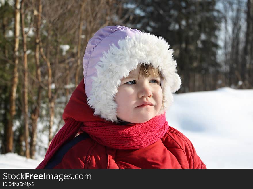 Little sad girl stands in winter forest and looks into distance