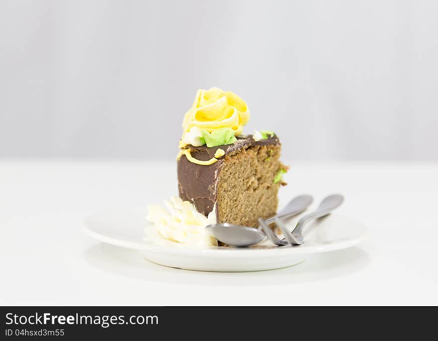 Slice of chocolate cake and fork in white plate on white background.