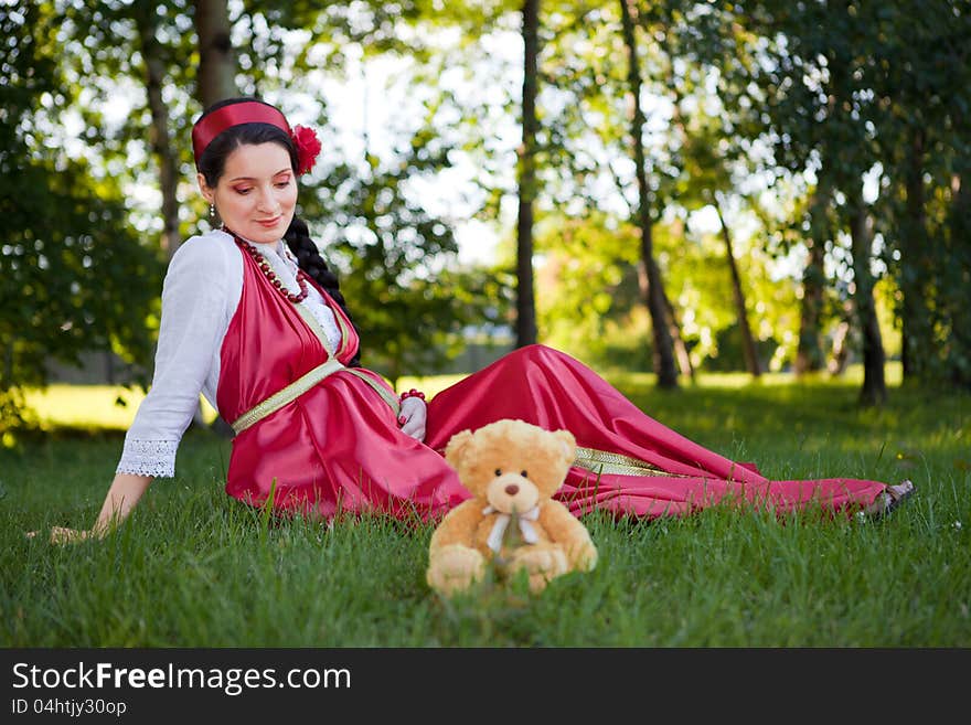 A young pregnant girl sitting on the grass in a red dress