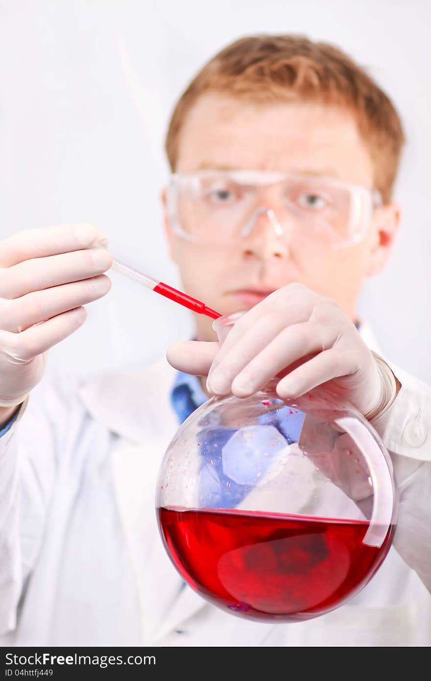 Man in white coat and protective glasses taking red sample from round flask. Man in white coat and protective glasses taking red sample from round flask