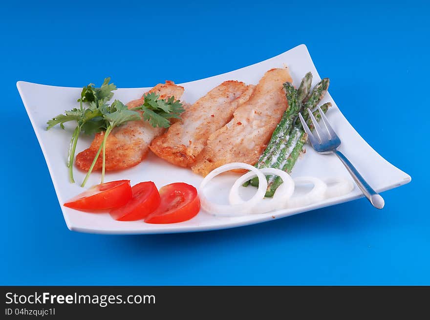 Fish fried in pastry with asparagus and tomatoes against a blue background. Fish fried in pastry with asparagus and tomatoes against a blue background