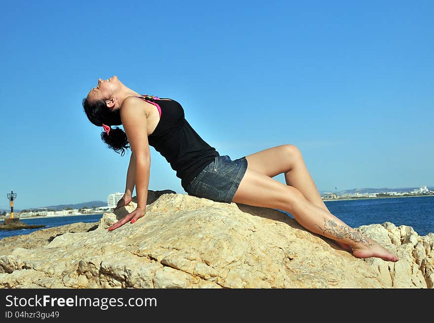 Young girl lying on the rocks on the beach face to the sun. Young girl lying on the rocks on the beach face to the sun