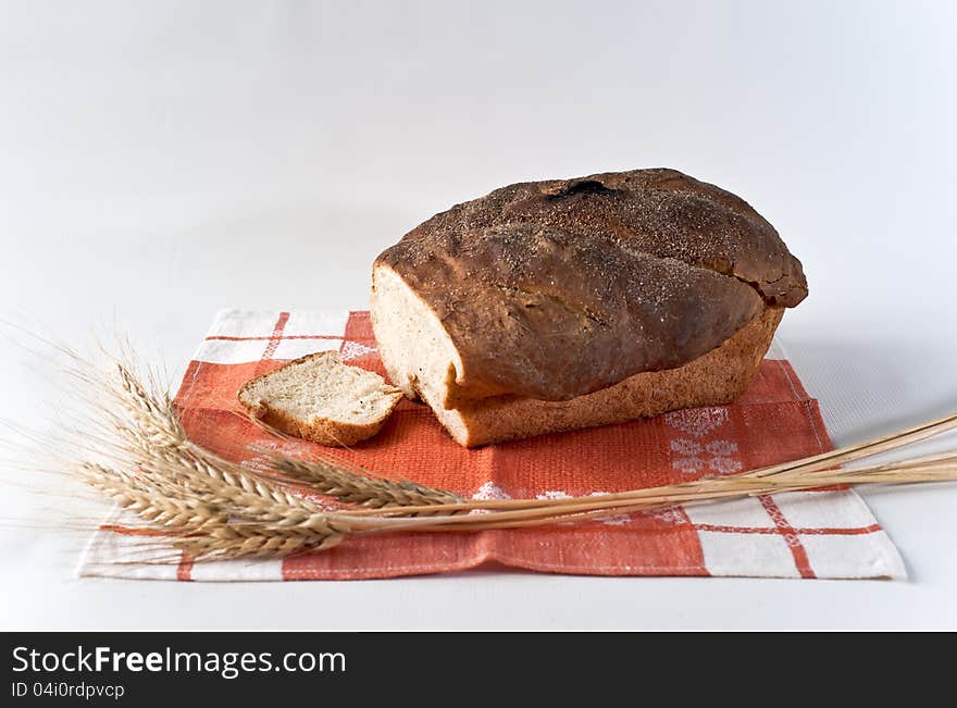 Loaf and slice of white wheat bread with wheatears on the red table-napkin. Loaf and slice of white wheat bread with wheatears on the red table-napkin