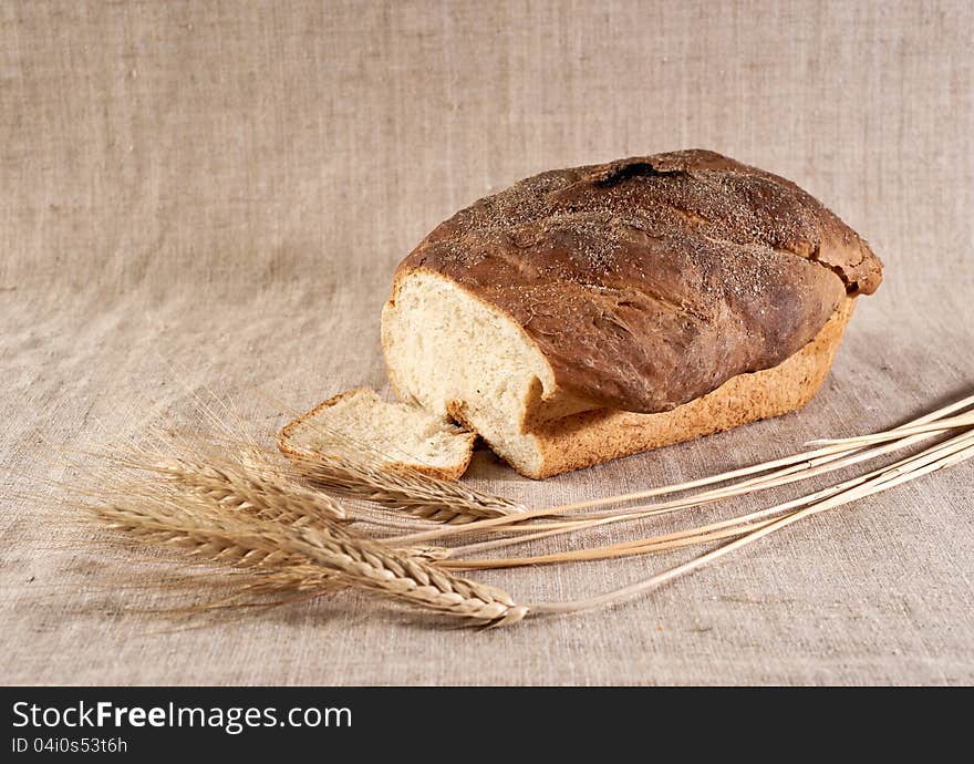 Loaf and slice of white wheat bread with wheatears on canvas. Loaf and slice of white wheat bread with wheatears on canvas