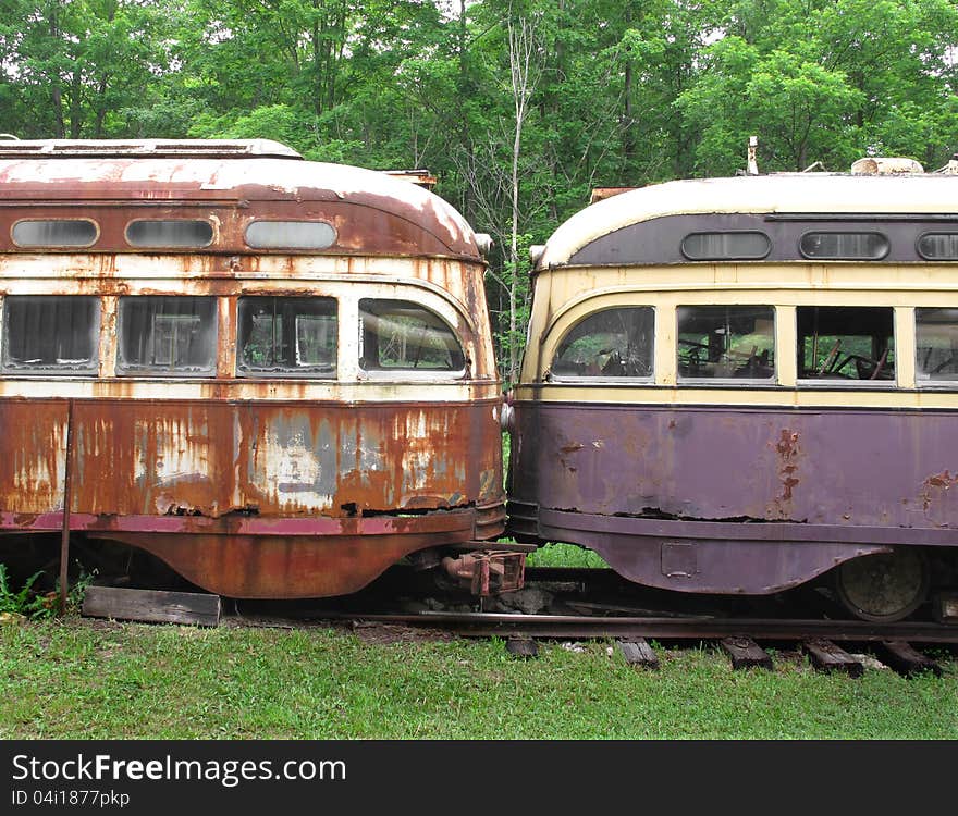 Close-up of the fronts of two old and weathered electric streetcars parked nose to nose in the woods. Close-up of the fronts of two old and weathered electric streetcars parked nose to nose in the woods.