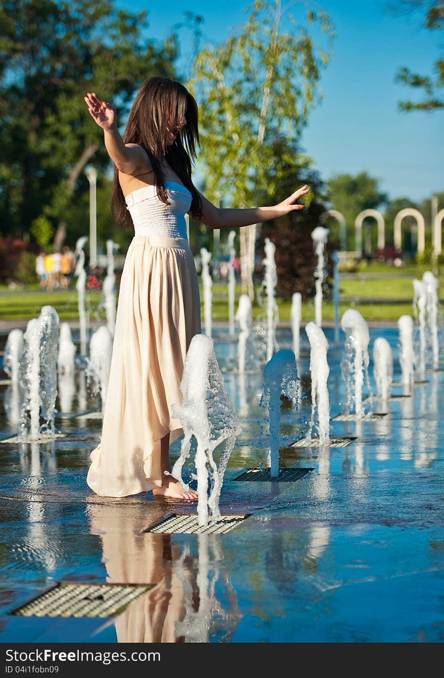 Young beautiful brunette girl playing at outdoor water fountain.Sunny day. Young beautiful brunette girl playing at outdoor water fountain.Sunny day