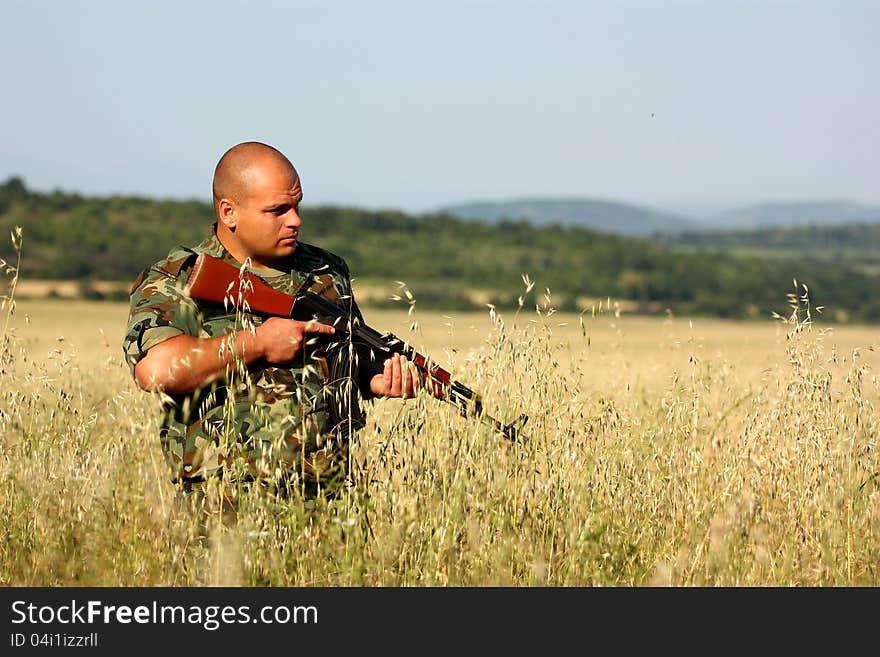 A soldier holding his assault-rifle (ak-47) on a open field.