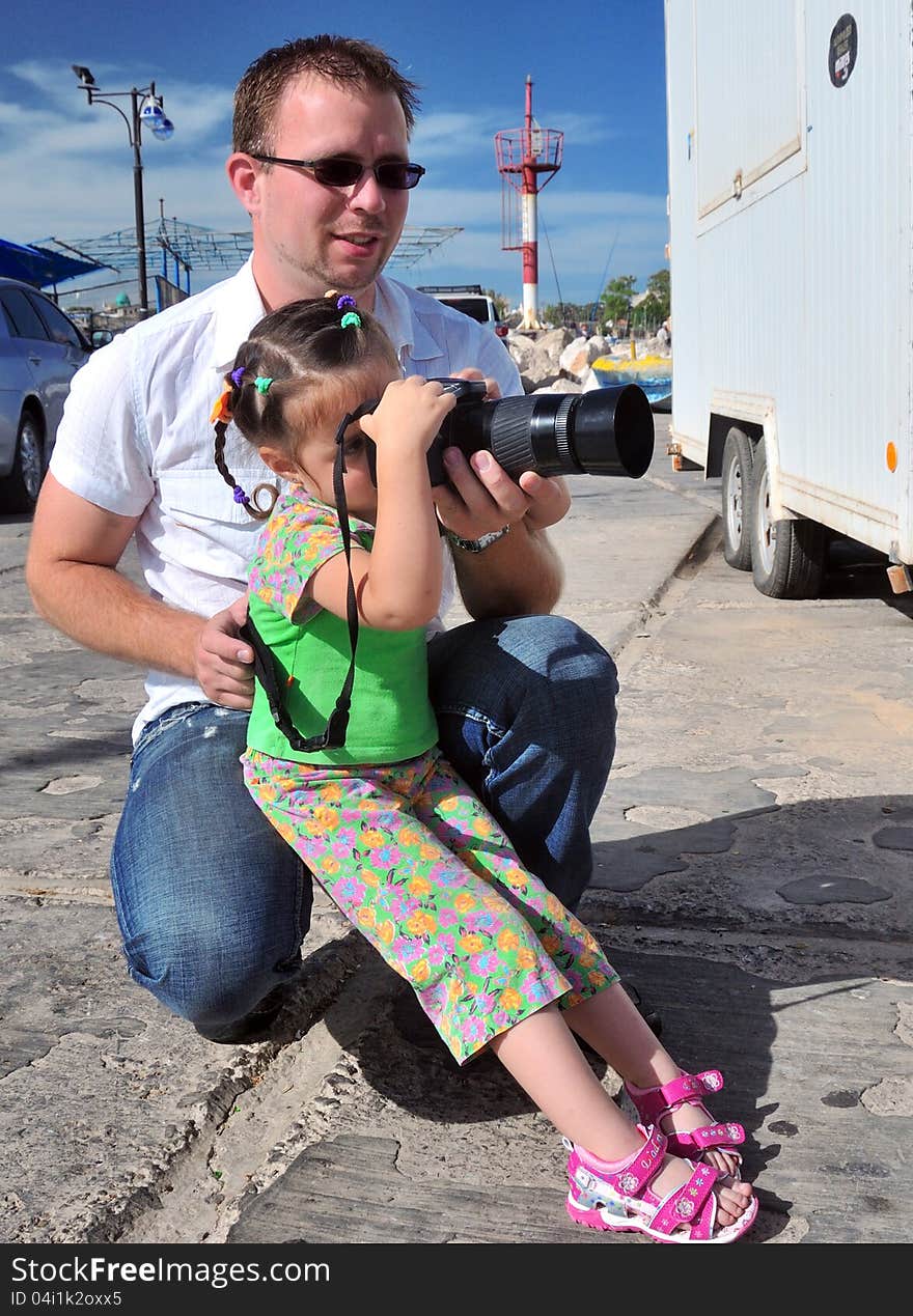 Dad teaches his daughter to photograph their camera, and maintains its bottom. Dad teaches his daughter to photograph their camera, and maintains its bottom