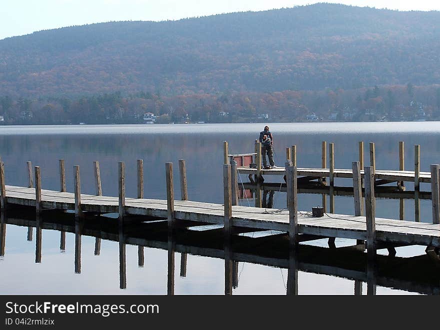 Solitary fisherman out in the early morning hours on a pier at the lake. Solitary fisherman out in the early morning hours on a pier at the lake.