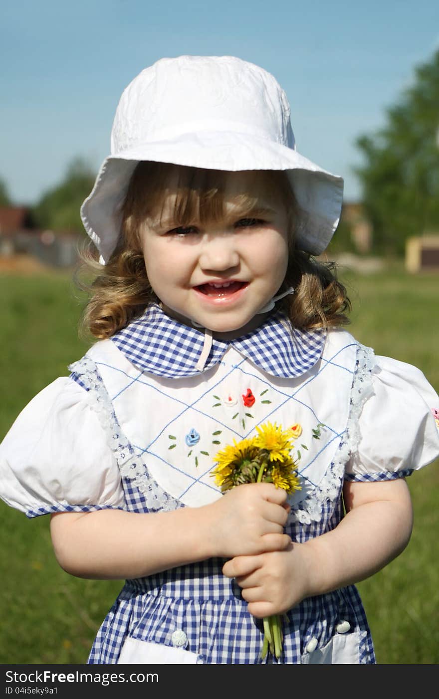 Beautiful little girl wearing dress holds yellow dandelions and looks at camera. Beautiful little girl wearing dress holds yellow dandelions and looks at camera