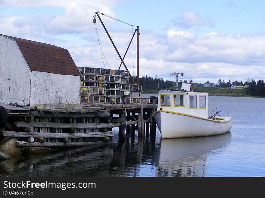 A small work boat is moored to a wooden wharf loaded with lobster pots. A small work boat is moored to a wooden wharf loaded with lobster pots.