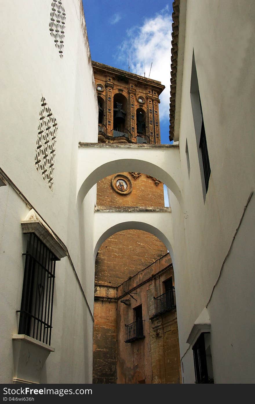 View of the tower of the church of Ronda from  a typical alley with arcs and white facades. View of the tower of the church of Ronda from  a typical alley with arcs and white facades.