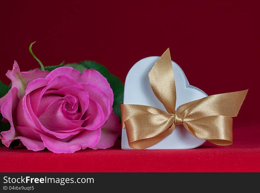 Heart shaped gift box with pink rose on red background. Heart shaped gift box with pink rose on red background