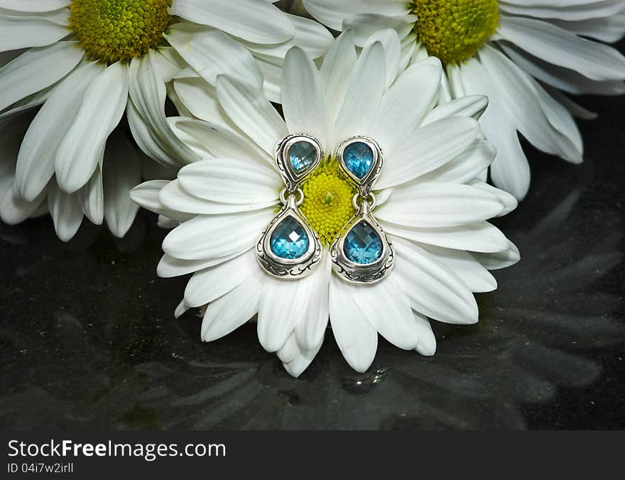 Blue topaz and sterling silver earrings displayed on a white gerbera daisy mounted on polished black granite. Blue topaz and sterling silver earrings displayed on a white gerbera daisy mounted on polished black granite