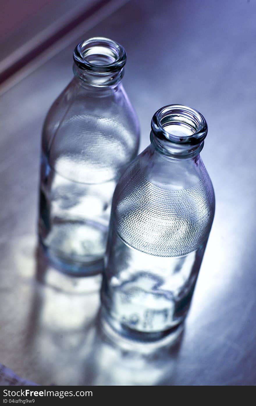 Two empty glass bottle on a mirrored table