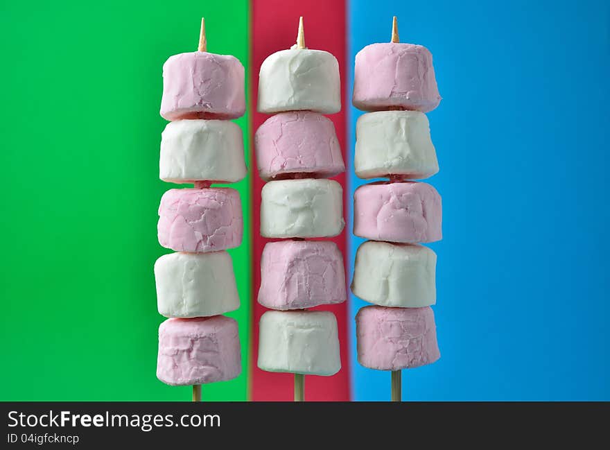 Pink and white marshmallows on skewers with a colorful background.