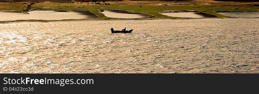 Traditional egyptian fisherman near a rowing boat on the Nile. Shot agaist the sun. Traditional egyptian fisherman near a rowing boat on the Nile. Shot agaist the sun